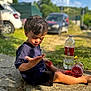 child, boy, outdoor, sitting, pavement, plastic_bottle, red_liquid, casual_clothing, shorts, short_sleeve_shirt, curious, daylight, car, greenery, sunlight, shadow, nature, summer, expression, hand