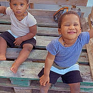 Ousmane participe au concours pour gagner de l'argent avec cette photo : child, toddler, smiling, serious, barefoot, wooden_bench, outdoor, casual_clothing, necklace, shorts, short_sleeve_shirt, wooden_floor, pallet, two_children, happy, cute, playful, sitting, friends, daylight