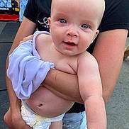 Richie is registered to the contest to win money with this photo: baby, child, infant, portrait, smiling, blue_eyes, bald, outdoor, held, adult, arms, blanket, lavender, diaper, clothing, close_up, face, happy, people, walkway