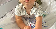 Richie joined the competition — help win amazing prizes! baby, child, infant, crib, nursery, portrait, sitting, wide_eyed, face, hands, striped_clothing, onesie, white_bedding, mesh, crib_sheet, toy, indoor, adorable, looking_at_camera, soft_lighting