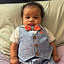 Dakota is registered to the contest to win money with this photo: baby, infant, child, curly_hair, bow_tie, vest, suit, striped_shirt, pants, socks, bed, pillow, blanket, wood_headboard, hands, portrait, indoors, cute, neutral_expression, rolled_pants