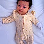 baby, infant, onesie, yellow_clothing, lying_down, blanket, cute, face, child, newborn, soft_lighting, portrait, sleepwear, small_hands, footed_pajamas, curly_hair, indoors, sleeping_area, adorable, peaceful