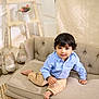 toddler, child, couch, sofa, blue_shirt, khaki_pants, barefoot, indoor, plush_toys, decor, rug, smiling, curly_hair, face, buttoned_shirt, home_interior, furniture, cute, portrait, seated