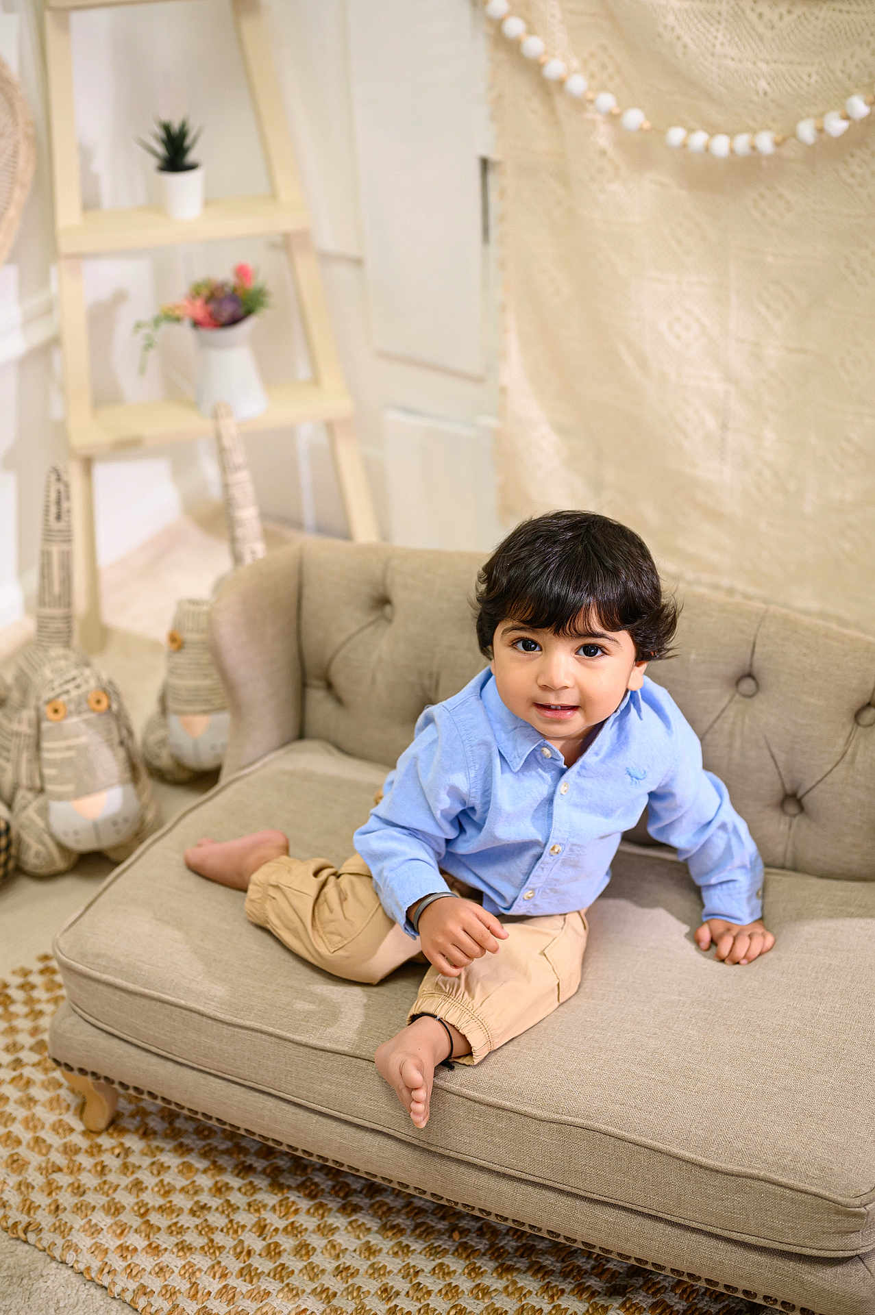 Gutaj Singh joined the competition — help win amazing prizes! toddler, child, couch, sofa, blue_shirt, khaki_pants, barefoot, indoor, plush_toys, decor, rug, smiling, curly_hair, face, buttoned_shirt, home_interior, furniture, cute, portrait, seated