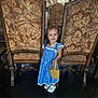 Amelia is registered to the contest to win money with this photo: child, girl, blue_dress, smile, basket, chair, pattern, wooden_furniture, indoors, floor, portrait, person, cute, happy, young_child, small_bag, footwear, white_shoes, standing, decor