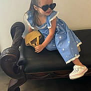 Amelia is registered to the contest to win money with this photo: child, girl, blue_dress, heart_shaped_sunglasses, wicker_bag, bench, wooden_furniture, leather_seat, indoor, floor, white_shoes, cute, fashion, portrait, smiling, casual, young, person, sitting, accessory