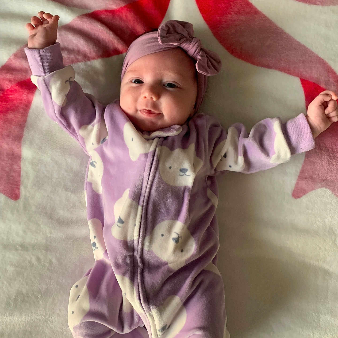 Ayla joined the competition — help win amazing prizes! arms_up, baby, blanket, child, comfortable, cozy, cute, face, happy, headband, indoors, infant, lying_down, onesie, playful, portrait, purple_clothing, sleepwear, smiling, soft_texture