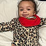 baby, infant, smile, curly_hair, leopard_print, onesie, red_bib, pillow, bed, lying_down, cute, happy, child, face, indoors, young_child, clothing, holiday, festive, portrait