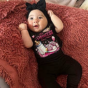 Lina participe au concours pour gagner de l'argent avec cette photo : baby, infant, black_clothing, headband, bow, blanket, pacifier_graphic, baby_bottle_graphic, pink_text, cute, smiling, lying_down, cozy, soft_texture, child, young, happy, indoors, person, small_feet