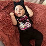 baby, infant, black_clothing, headband, bow, blanket, pacifier_graphic, baby_bottle_graphic, pink_text, cute, smiling, lying_down, cozy, soft_texture, child, young, happy, indoors, person, small_feet