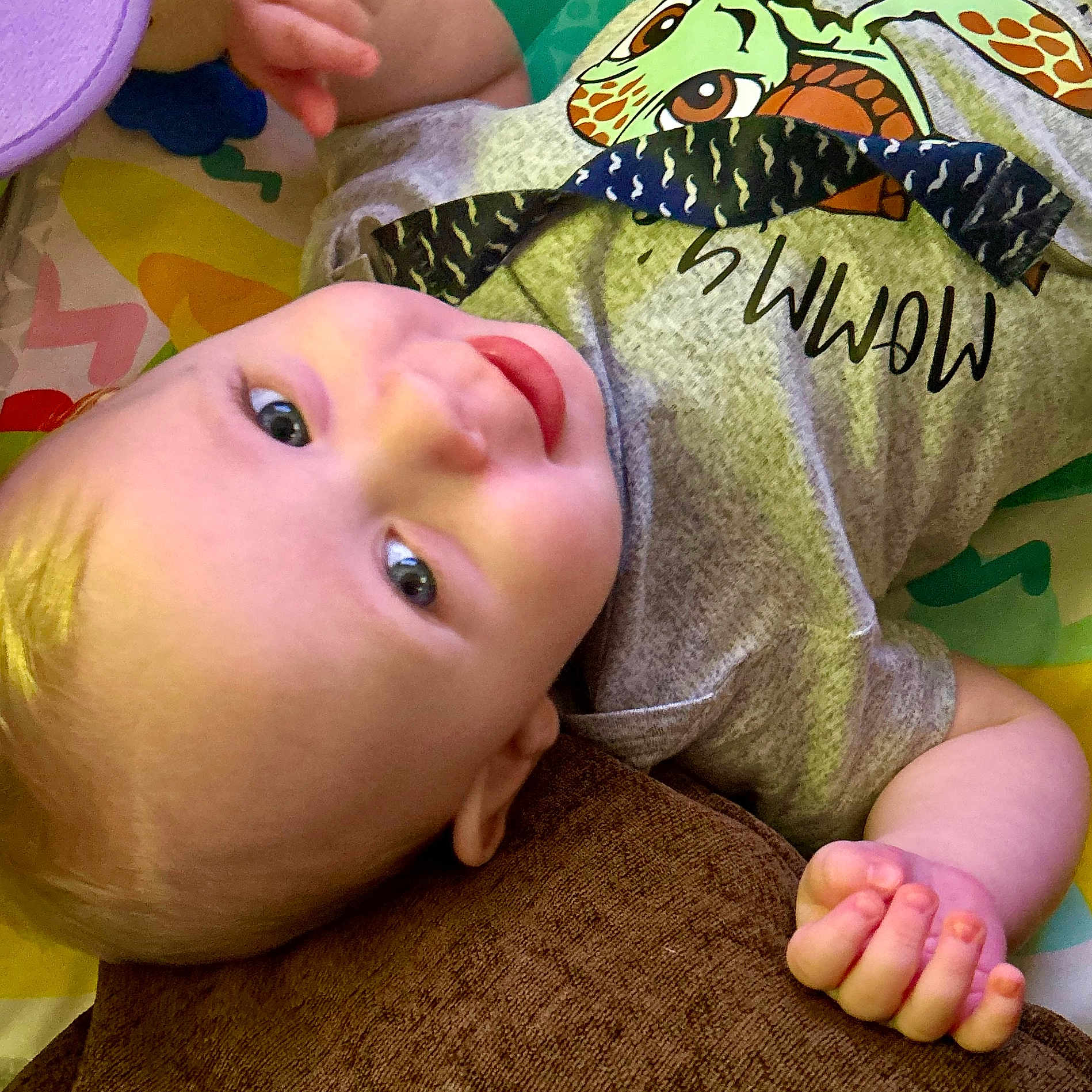 Jaxxon joined the competition — help win amazing prizes! baby, casual_clothing, child, colorful_play_mat, cute, eyes, face, gray_shirt, hand, happy, indoors, infant, lying_down, natural_light, portrait, relaxed, skin, smiling, turtle_graphic, young_child