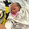 Sanai is registered to the contest to win money with this photo: baby, infant, blanket, swaddled, minion, cartoon, polka_dot, pink_clothing, face, head, soft_texture, cozy, lying_down, child, newborn, cute, indoor, warm, resting, wrapped