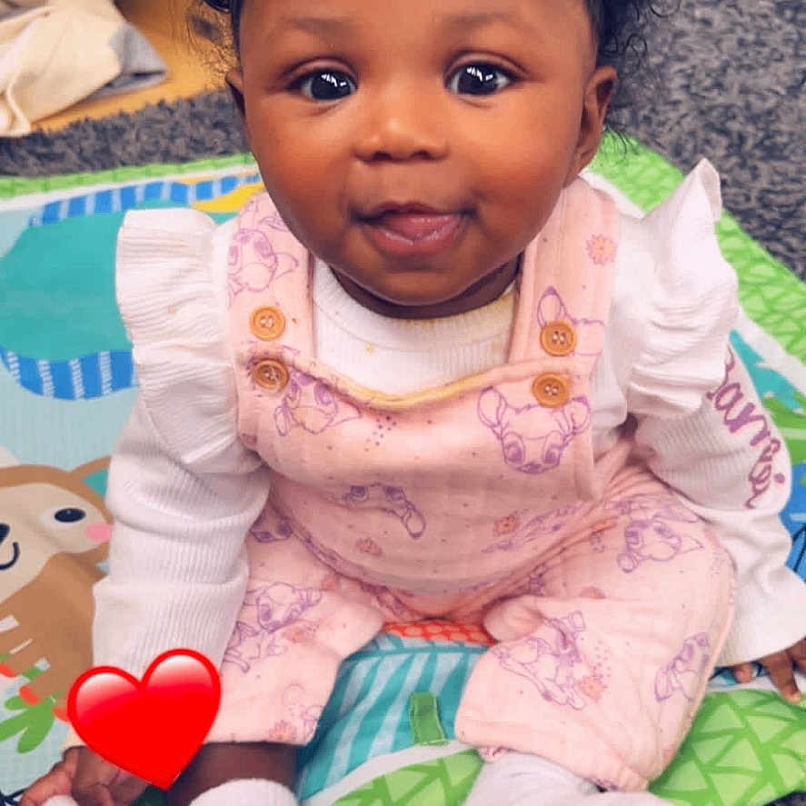 Jycee is registered to the contest to win money with this photo: baby, child, curly_hair, pink_overalls, white_socks, play_mat, indoor, smiling, cute, bright_eyes, floor, carpet, toy, sitting, portrait, infant, happy, toddler, cozy, room