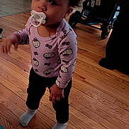 Arianna joined the competition — help win amazing prizes! toddler, child, pacifier, purple_bow, hello_kitty, long_sleeve_shirt, black_pants, socks, wooden_floor, indoor, stroller, doorway, person, standing, flooring, social_media_overlay, text_overlay, baby, cute, home