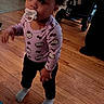 toddler, child, pacifier, purple_bow, hello_kitty, long_sleeve_shirt, black_pants, socks, wooden_floor, indoor, stroller, doorway, person, standing, flooring, social_media_overlay, text_overlay, baby, cute, home