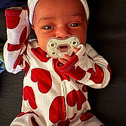Denver joined the competition — help win amazing prizes! baby, infant, pacifier, onesie, heart_pattern, hat, sleepwear, red_and_white, lying_down, portrait, cute, small_hands, fabric, eyes, face, skin, sofa, closeup, hand, bokeh