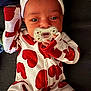 baby, infant, pacifier, onesie, heart_pattern, hat, sleepwear, red_and_white, lying_down, portrait, cute, small_hands, fabric, eyes, face, skin, sofa, closeup, hand, bokeh