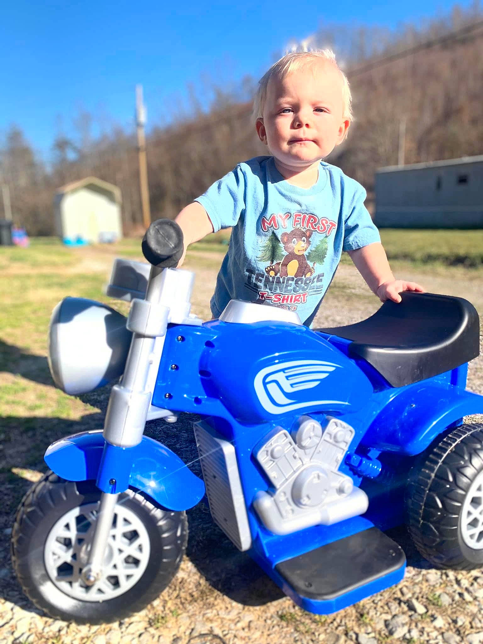 Bentlee is registered to the contest to win money with this photo: alloy_wheel, automotive_design, automotive_tire, automotive_wheel_system, fender, grass, happy, mode_of_transport, motor_vehicle, person, riding_toy, rim, rolling, sky, synthetic_rubber, t_shirt, tire, toddler, tread, vehicle