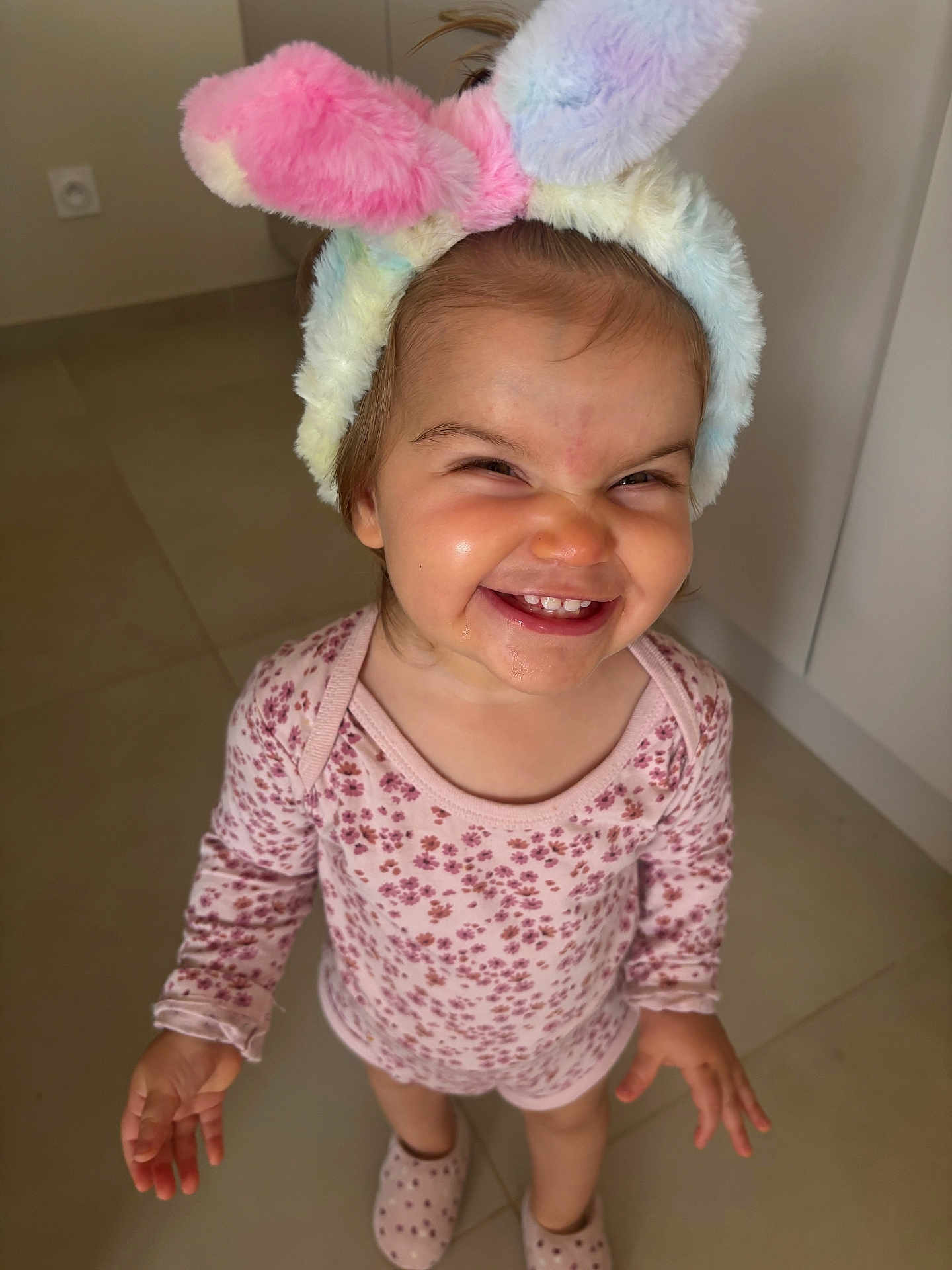 Vaeena participe au concours pour gagner de l'argent avec cette photo : toddler, child, smiling, bunny_ears, headband, floral_outfit, indoors, floor, tiles, happy, cute, person, young_child, playful, fashion, footwear, slippers, portrait, expression, baby