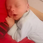 Enzo participe au concours pour gagner de l'argent avec cette photo : baby, sleeping, newborn, person, white_clothing, red_shirt, bed, indoor, peaceful, infant, face, head, hand, resting, cozy, soft_lighting, closeup, portrait, child, human