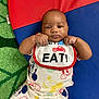 baby, infant, bib, mickey_mouse, clothing, colorful, play_mat, green_carpet, red, blue, yellow, cute, smiling, child, person, portrait, lying_down, hands, raised_fists, indoor