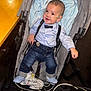 baby, child, stroller, medical_tubes, nasal_cannula, blue_blanket, bow_tie, suspenders, denim_pants, shoes, smiling, indoor, person, infant, cute, healthcare, happy, seated, clothing, footwear