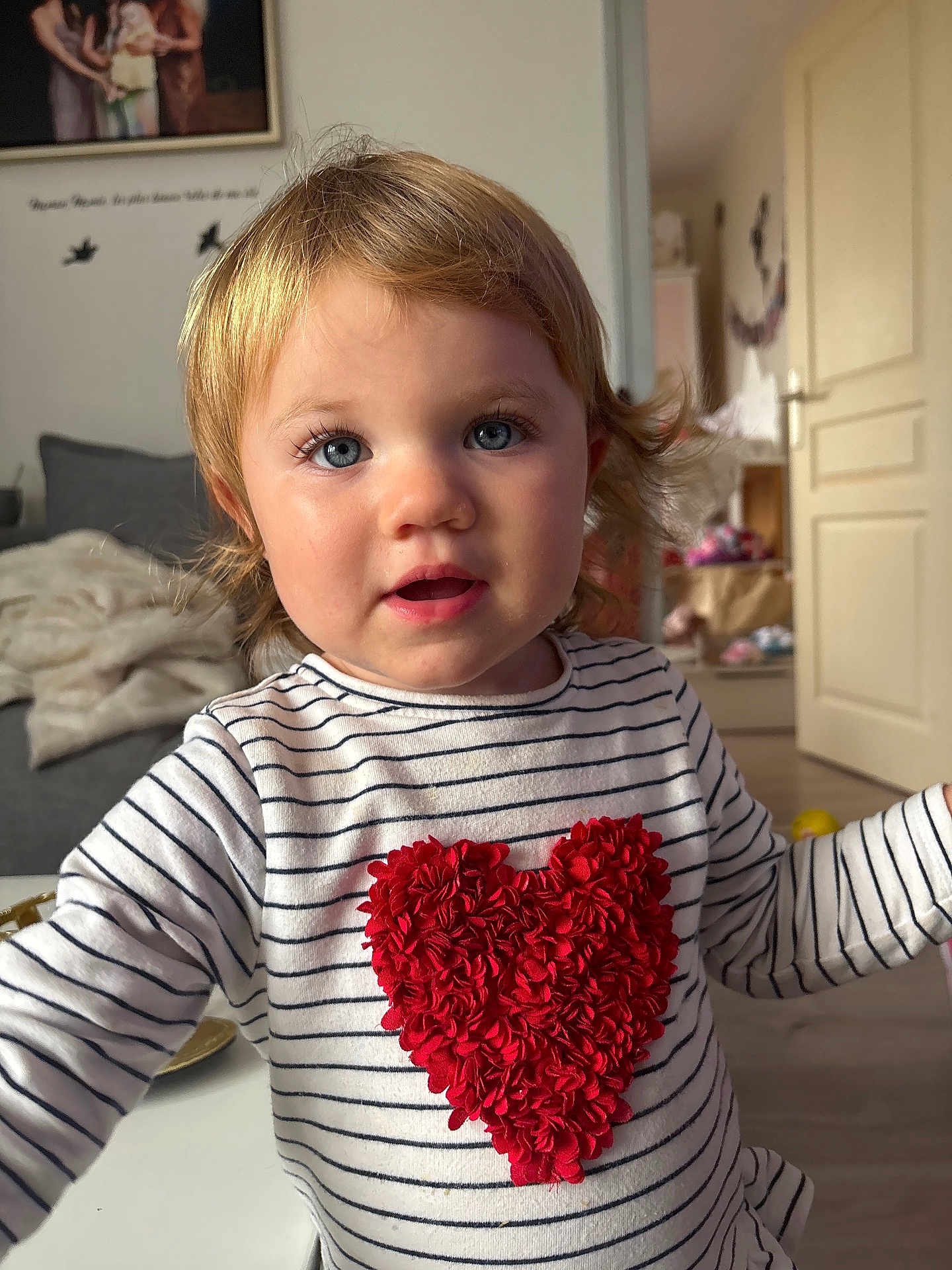 Lana a rejoint le concours — aidez-le/la à gagner de superbes lots ! toddler, child, face, blue_eyes, blonde_hair, striped_shirt, red_heart, indoor, living_room, furniture, door, soft_light, portrait, cute, young_child, person, smiling, expression, home, cozy