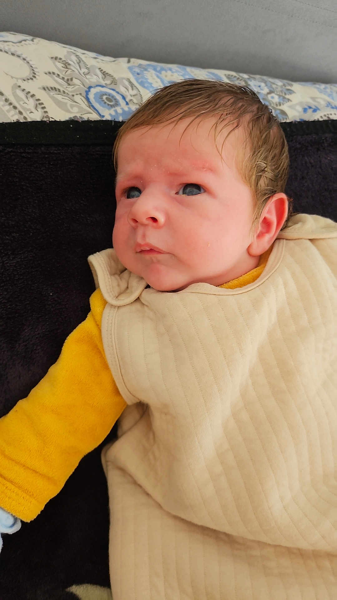 Lamri participe au concours pour gagner de l'argent avec cette photo : baby, infant, face, clothing, yellow_sleeve, blanket, portrait, person, cute, cozy, young_child, indoors, skin, head, expression, eyes, hair, lying_down, warm, soft
