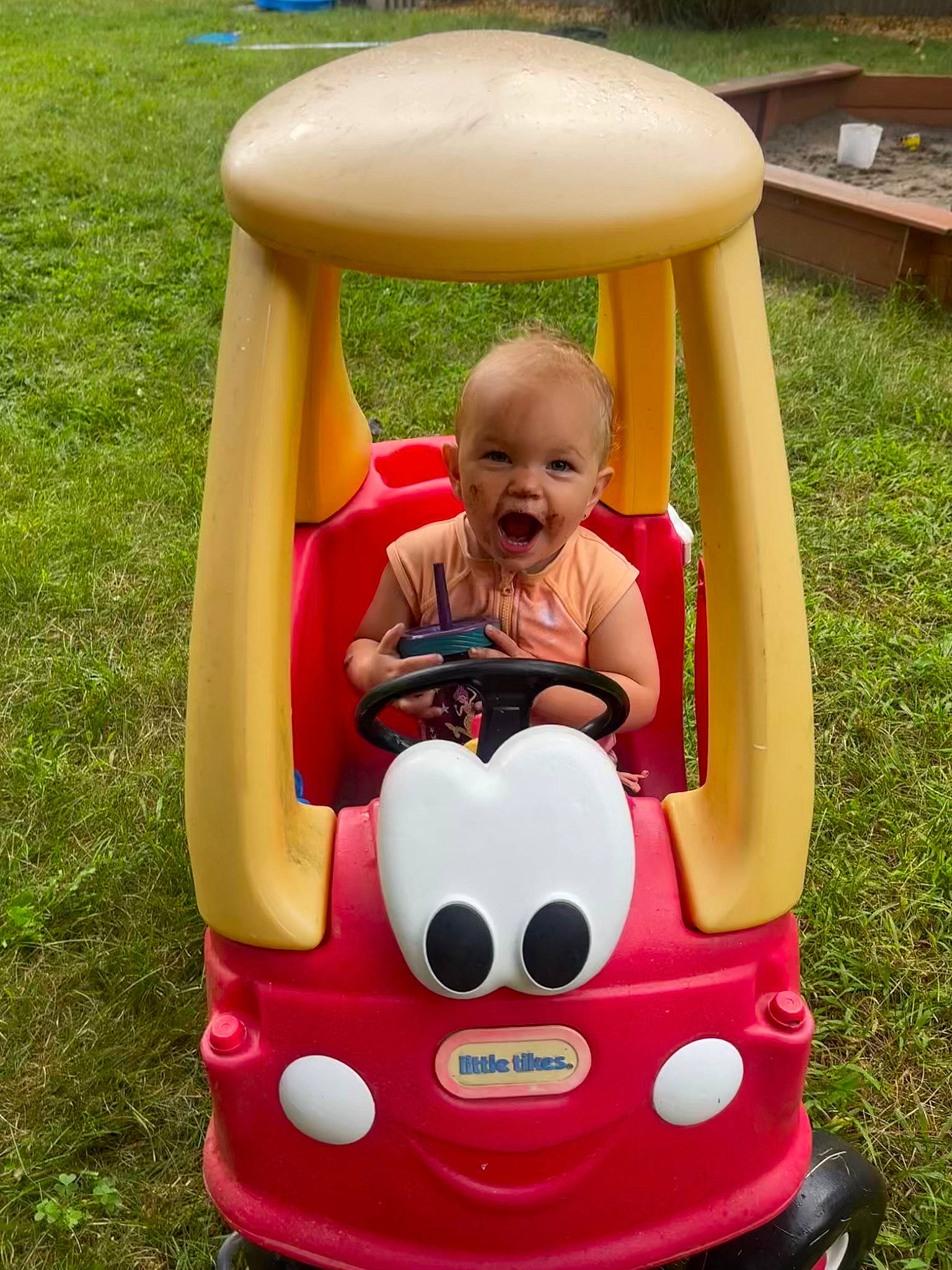 Kenzie is registered to the contest to win money with this photo: baby, baby_toddler_clothing, bumper, child, fun, grass, green, happy, head, leisure, motor_vehicle, person, photograph, plant, product, recreation, red, riding_toy, smile, snapshot