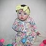 Brynlee is registered to the contest to win money with this photo: baby, child, headband, yellow, onesie, floral_pattern, plastic_eggs, pastel_colors, sitting, curious, blue_eyes, indoor, neutral_background, infant, cute, portrait, soft_texture, colorful, playtime, young_child
