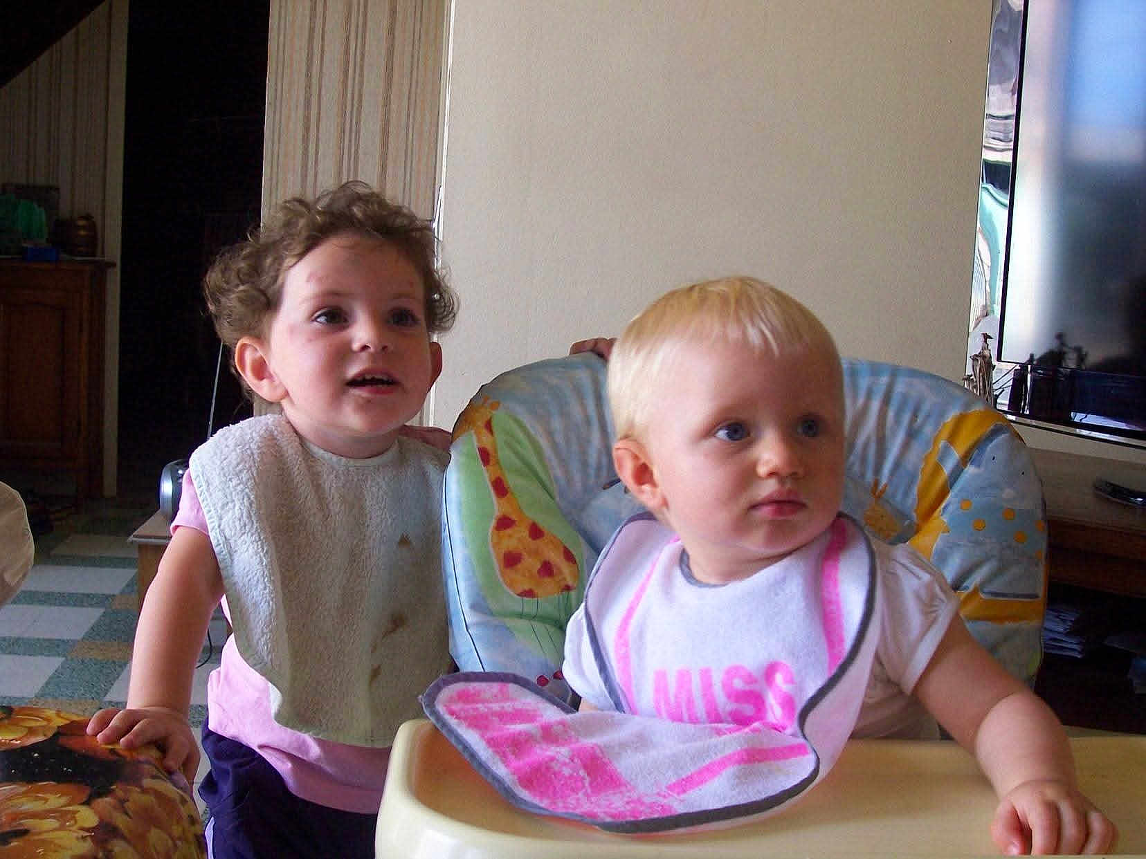 Milene a rejoint le concours — aidez-le/la à gagner de superbes lots ! child, toddler, bib, high_chair, curly_hair, blonde, indoor, furniture, television, table, clothing, person, baby, face, expression, curiosity, home, floor, hand, seat