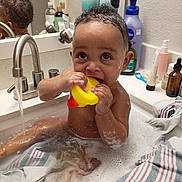 Mossiah is registered to the contest to win money with this photo: baby, bath, bathtub, bubbles, child, curly_hair, face, foam, faucet, mirror, plastic_toy, rubber_duck, sink, soap, striped_towel, water, wet_skin, young_child, bathroom, personal_care