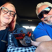 Niner is registered to the contest to win money with this photo: black_dog, car_interior, casual_clothing, checkered_pattern, couple, dog, fun, hand, happy, indoors, man, pet_carrier, portrait, reflection, road_trip, smiling, summer, sunglasses, travel, woman