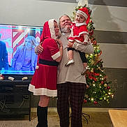 Novalee is registered to the contest to win money with this photo: family, christmas, holiday, tree, decorations, toddler, man, woman, santa_claus_costume, boots, living_room, television, happy, celebration, indoor, smiling, holding, festive, pajamas, floor