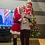 family, christmas, holiday, tree, decorations, toddler, man, woman, santa_claus_costume, boots, living_room, television, happy, celebration, indoor, smiling, holding, festive, pajamas, floor