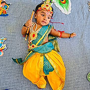 Revansh Reddy is registered to the contest to win money with this photo: baby, child, costume, traditional_clothing, peacock_feather, jewelry, blue_blanket, yellow_pants, toy, stick, cute, indian_culture, face_paint, headband, lying_down, colorful, indoors, decorations, celebration, infant