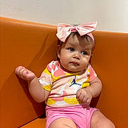 Lina a rejoint le concours — aidez-le/la à gagner de superbes lots ! baby, child, infant, pink_shorts, colorful_shirt, headband, bow, orange_couch, sitting, indoor, cute, curious, chubby_cheeks, portrait, clothing, skin, person, young, expression, casual