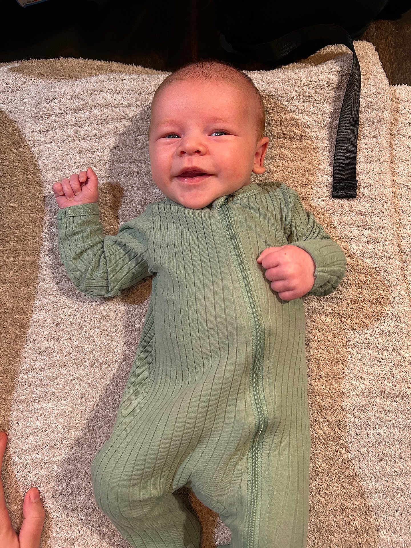Ashton is registered to the contest to win money with this photo: baby, infant, smiling, green_onesie, carpet, hand, fist, cute, lying_down, happy, child, portrait, indoor, cozy, soft_texture, young, playful, human, person, clothing