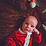 baby, black_belt, blanket, buttoned_shirt, candid, child, cozy, cute, festive, holiday_clothing, holiday_theme, indoor, infant, plush_teddy_bear, portrait, red_outfit, resting, santa_hat, soft_texture, warm_lighting