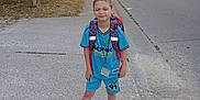 Christopher is registered to the contest to win money with this photo: backpack, blue_clothing, boy, car, casual, child, concrete, daylight, house, outdoor, person, pose, sidewalk, sneakers, street, suburban, summer, tree, urban, young