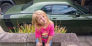 Isabella joined the competition — help win amazing prizes! child, girl, blonde_hair, pink_shirt, jeans, pink_shoes, concrete, grass, green_car, green_suv, carport, outdoor, plants, smiling, posing, casual, daylight, nature, playful, vehicle