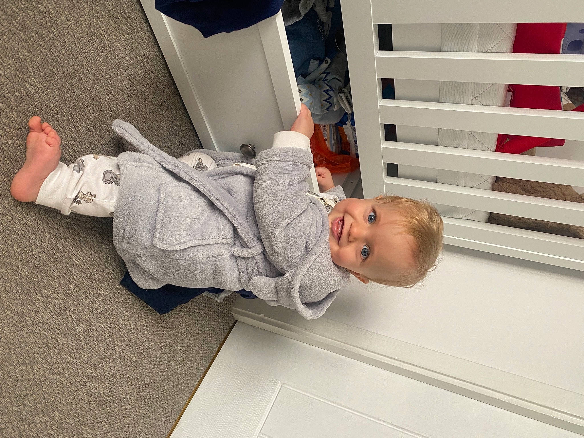 Eddie is registered to the contest to win money with this photo: baby, baby_products, baby_toddler_clothing, child, comfort, flooring, foot, fun, hat, headgear, house, human_leg, knee, nap, person, room, sandal, sitting, standing, toddler