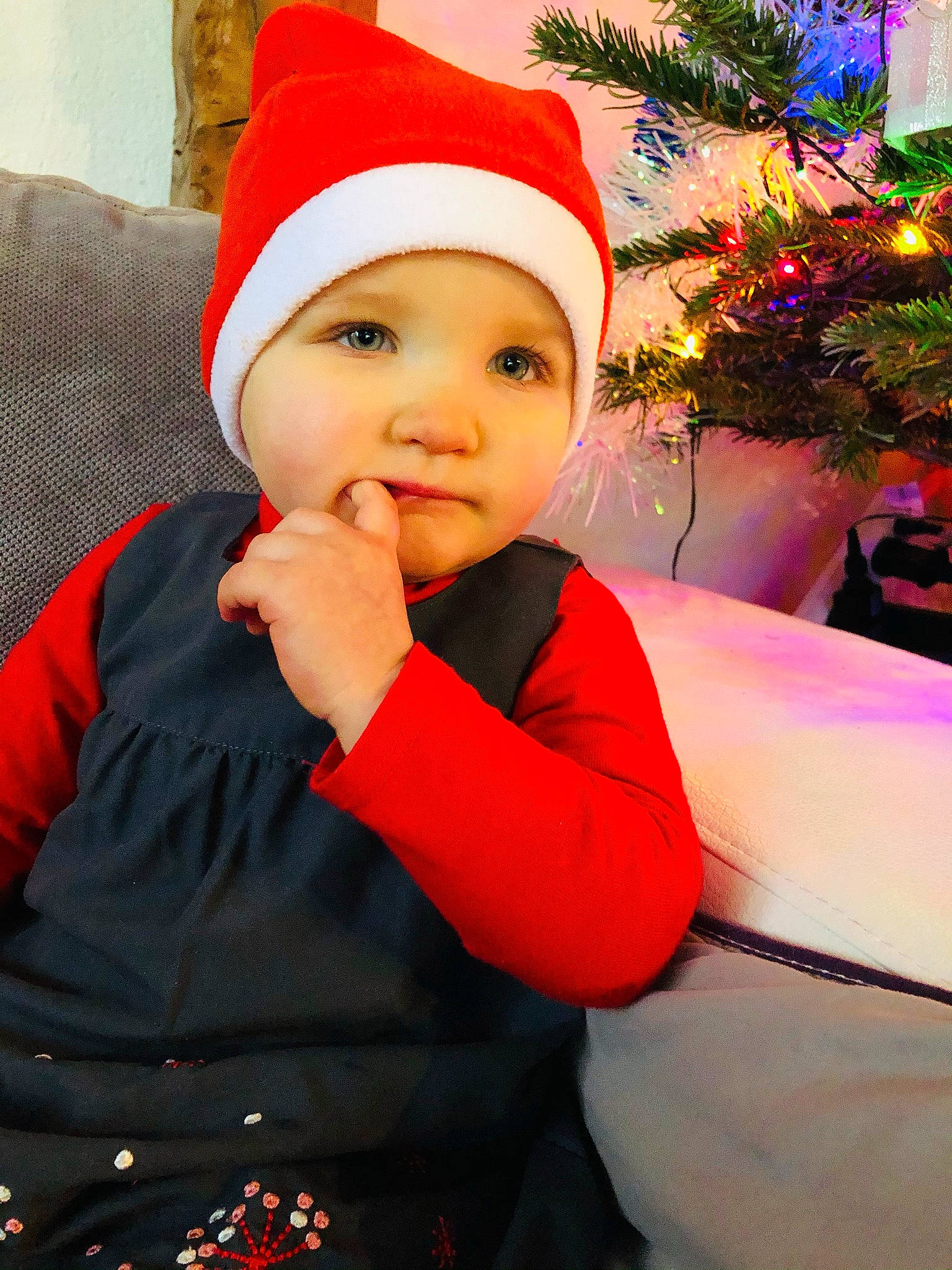Ophélie participe au concours pour gagner de l'argent avec cette photo : baby, baby_toddler_clothing, bonnet, christmas, christmas_decoration, christmas_eve, christmas_lights, conifer, costume, costume_accessory, costume_hat, couch, fictional_character, fir, fur, headwear, holiday, person, pleased, red