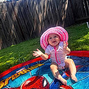 Nyleia is registered to the contest to win money with this photo: baby, child, pool, water, sunhat, pink, white_onesie, spiderman, superhero, outdoor, grass, fence, sunlight, shadow, happy, splashing, summer, play, smile, fun