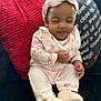 Harmony is registered to the contest to win money with this photo: baby, child, infant, pink_clothing, headband, couch, pillow, red_pillow, text_pillow, indoor, cute, smile, sitting, footwear, soft_toys, home, person, portrait, cozy, furniture