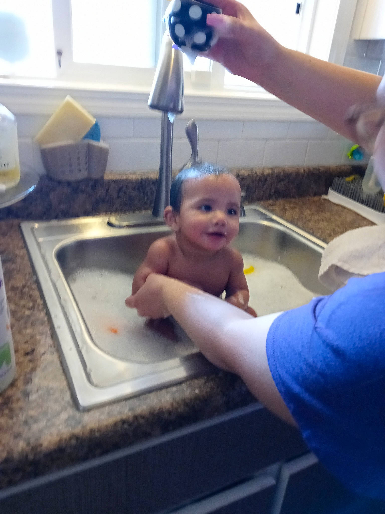 Ronin is registered to the contest to win money with this photo: arm, baby, bathing, chest, child, cooking, elbow, finger, fun, gesture, hand, kitchen, kitchen_sink, person, serveware, sink, table, tap, thumb, toddler