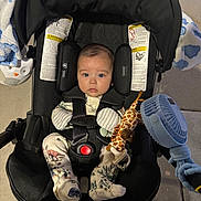 Dominic joined the competition — help win amazing prizes! baby, car_seat, infant, toy, giraffe, blue_fan, pajamas, dinosaur_pattern, face, child, sitting, clothing, safety_harness, indoor, blanket, cute, expression, head_support, footwear, person