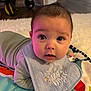 Dominic is registered to the contest to win money with this photo: baby, infant, face, bib, play_mat, indoor, floor, clothing, child, person, eyes, hair, expression, cute, toddler, carpet, soft_lighting, young, lying_down, portrait