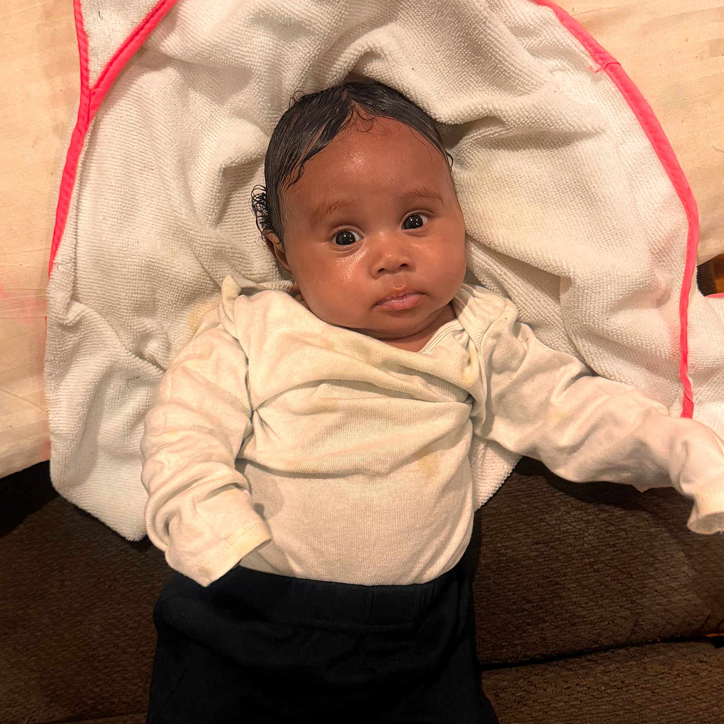 Legacy Howard joined the competition — help win amazing prizes! baby, big_eyes, black_pants, child, clothing, cream_top, curious, cute, fabric, face, indoors, infant, lying_down, person, portrait, relaxed, soft_texture, towel, white_towel, young_child