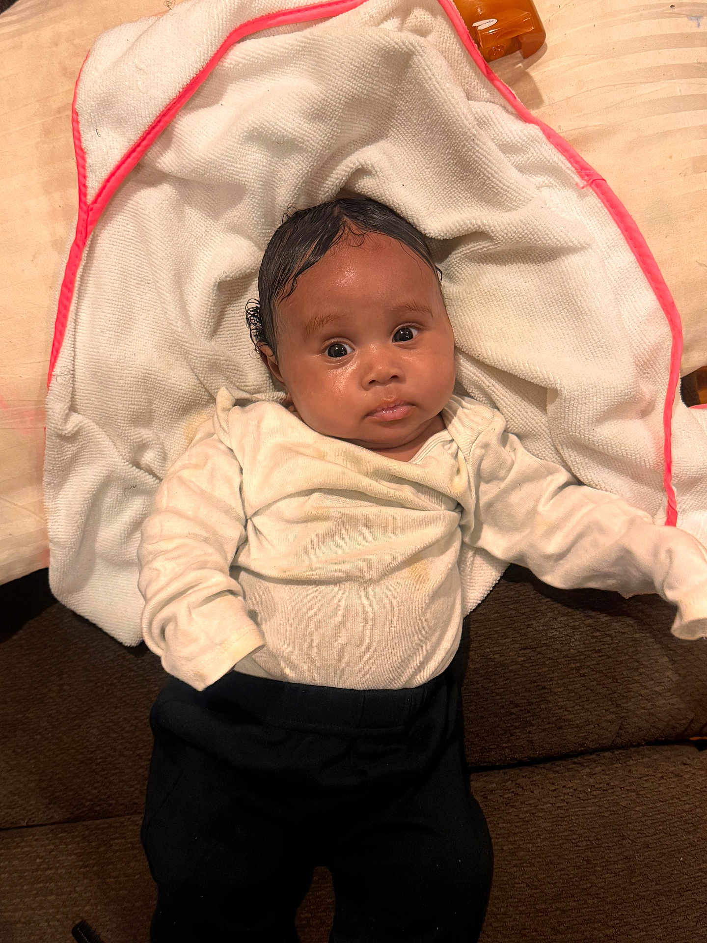 Legacy Howard joined the competition — help win amazing prizes! baby, infant, face, towel, white_towel, clothing, cream_top, black_pants, indoors, lying_down, person, cute, curious, young_child, child, soft_texture, fabric, relaxed, big_eyes, portrait